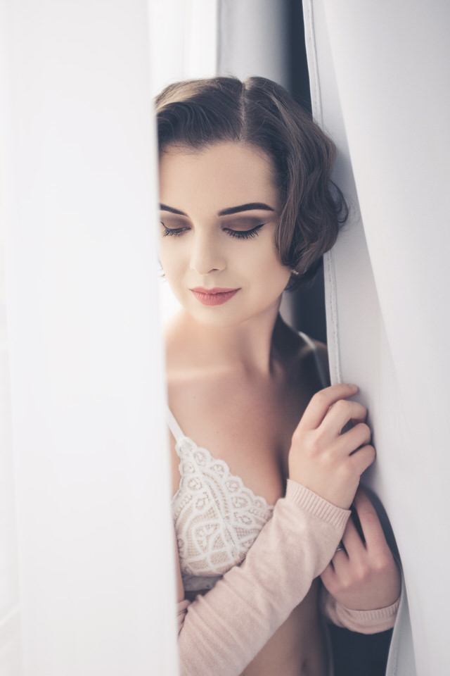 A photo of a woman standing in between some curtains in bridal lingerie