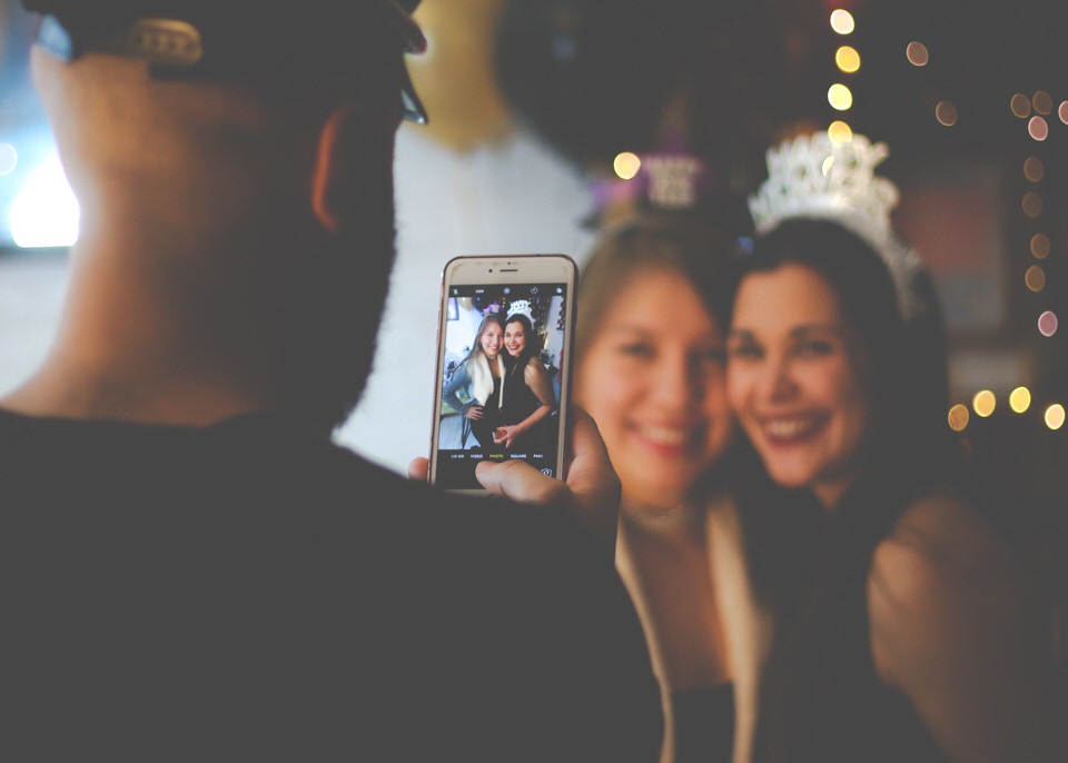 A photo of a man taking a photo of two girls on an iphone