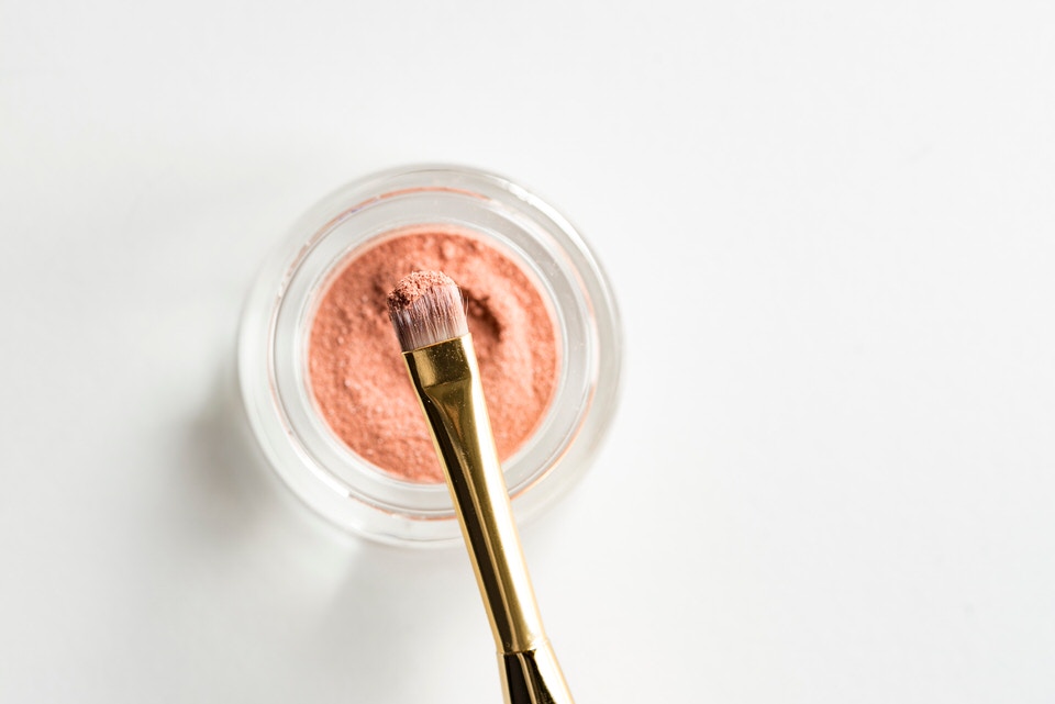 A flat lay image of an eyeshadow pot and makeup brush