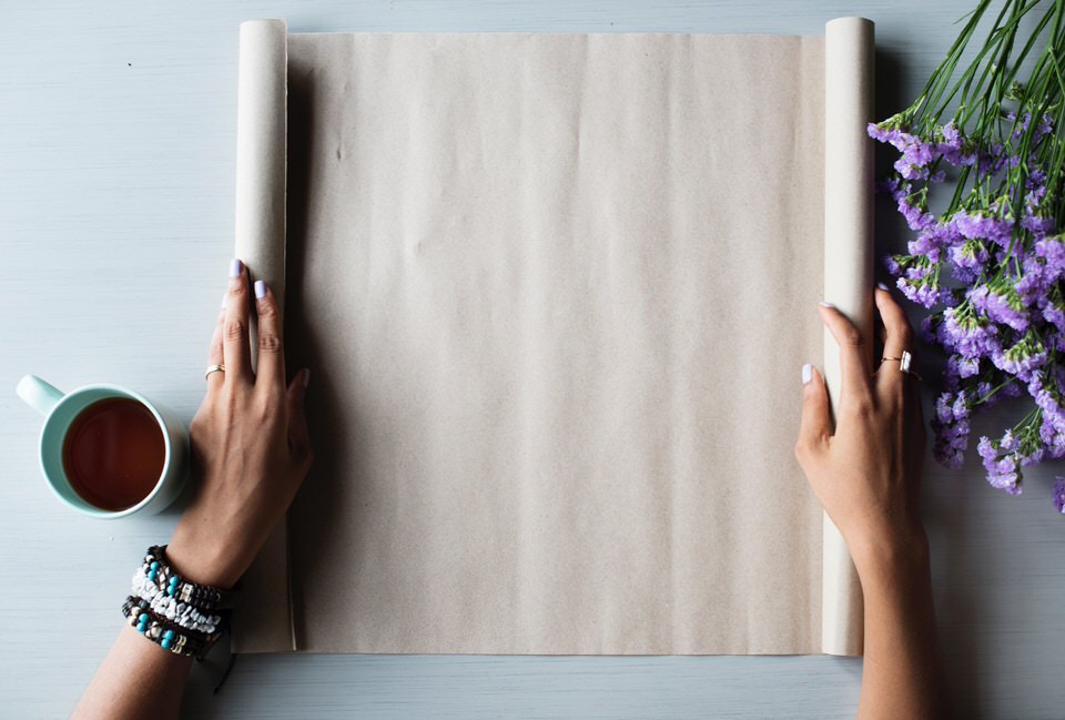 Flat lay image of a scroll of paper, flowers and a cup of tea